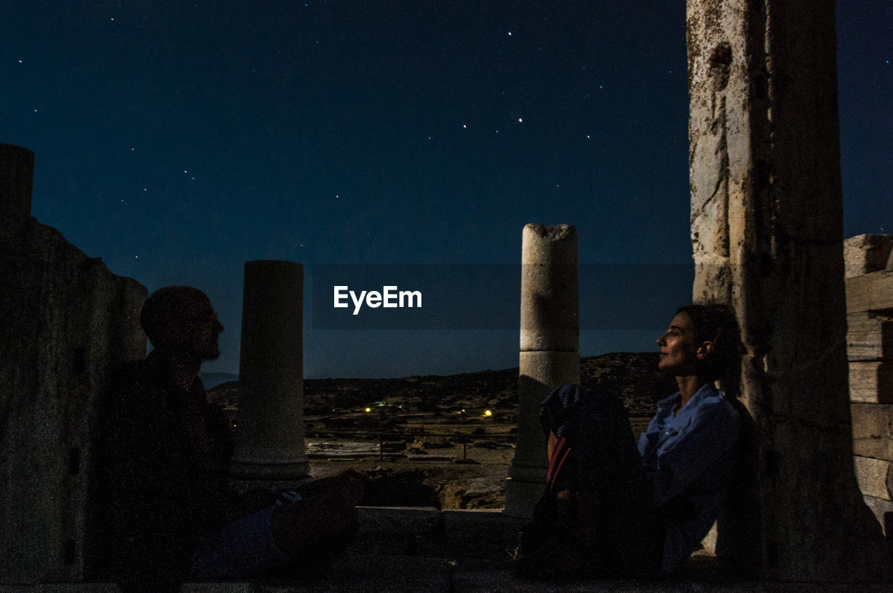 Friends sitting in old ruin against star field at night