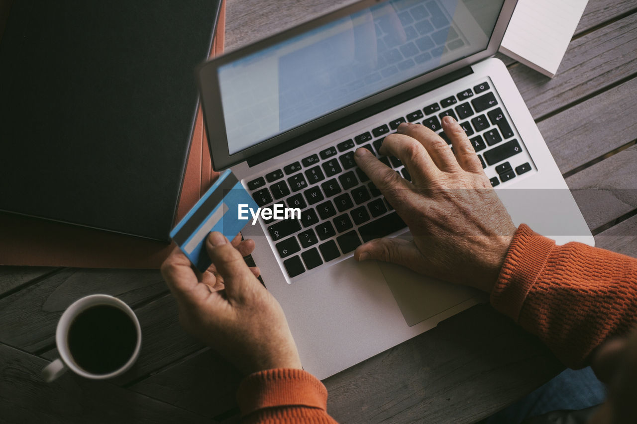 Senior man's hands doing online payment with credit card through laptop at home