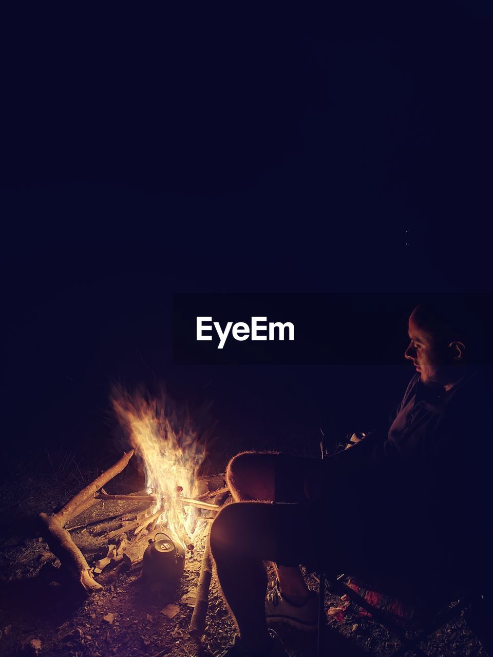 Side view of man sitting by campfire in dark at night