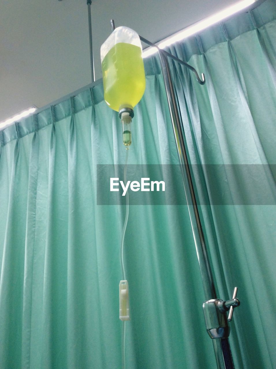 Low angle view of iv drip bag hanging by green curtain in hospital