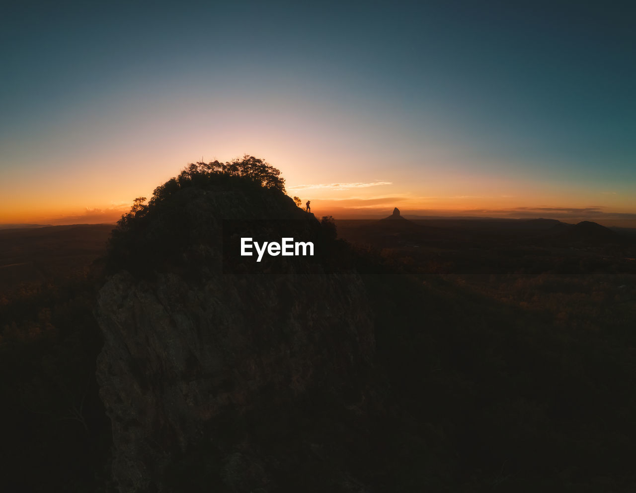 Silhouette of person on mountain edge photographing dramatic sunset landscape