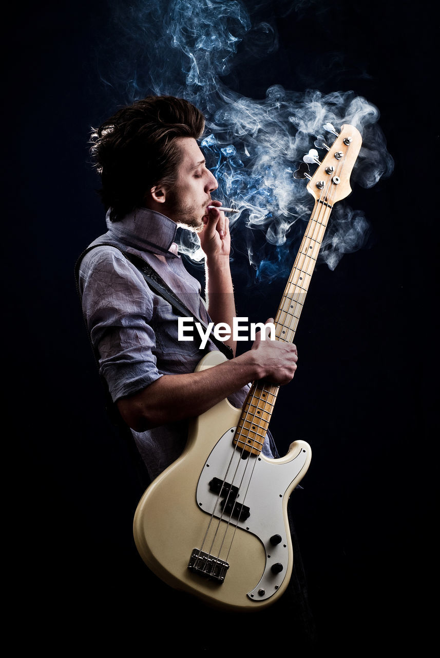 Portrait of a man with a guitar and a cigarette on a dark background and a light blue shirt