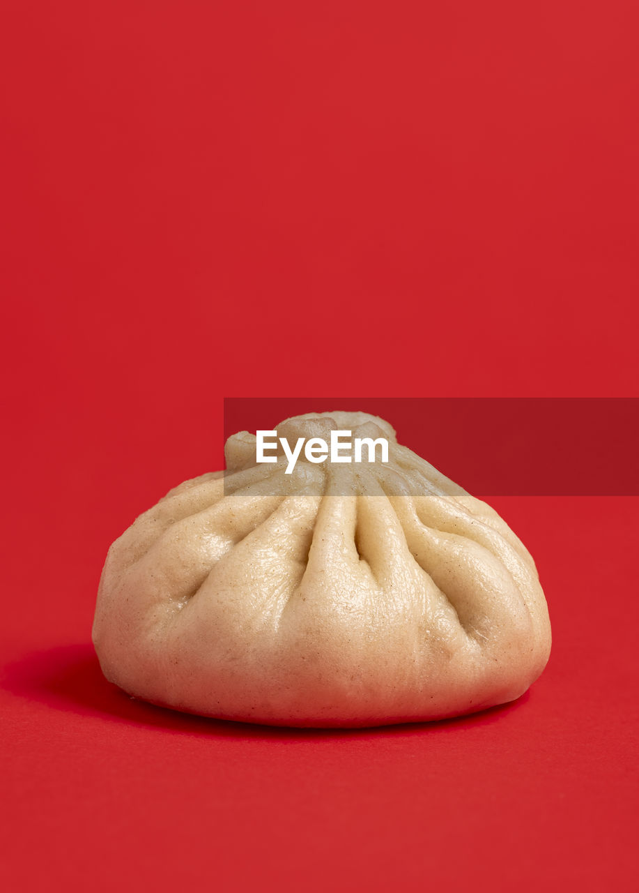 Close-up with a single bao dumpling isolated on a red colored background. homemade bao with meat.