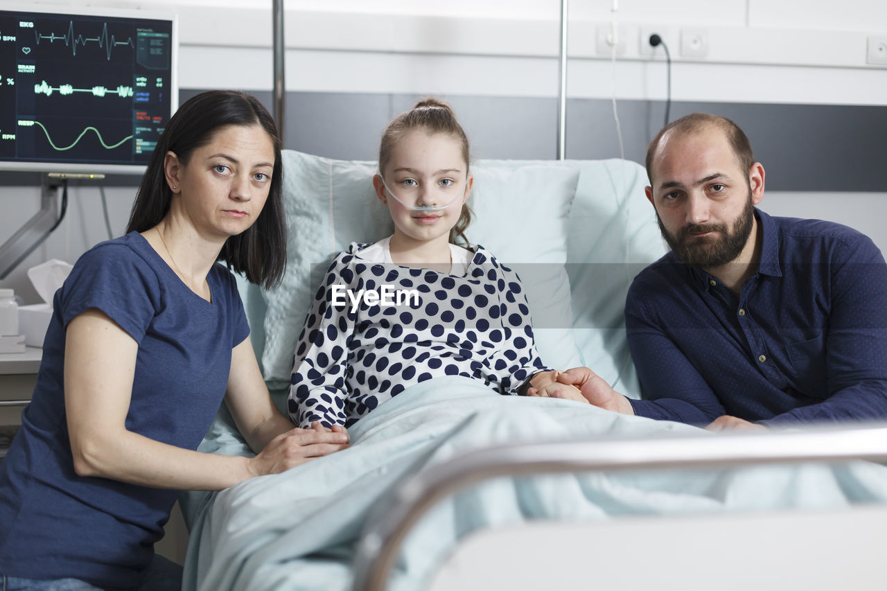 Parents with daughter sitting on bed in hospital ward