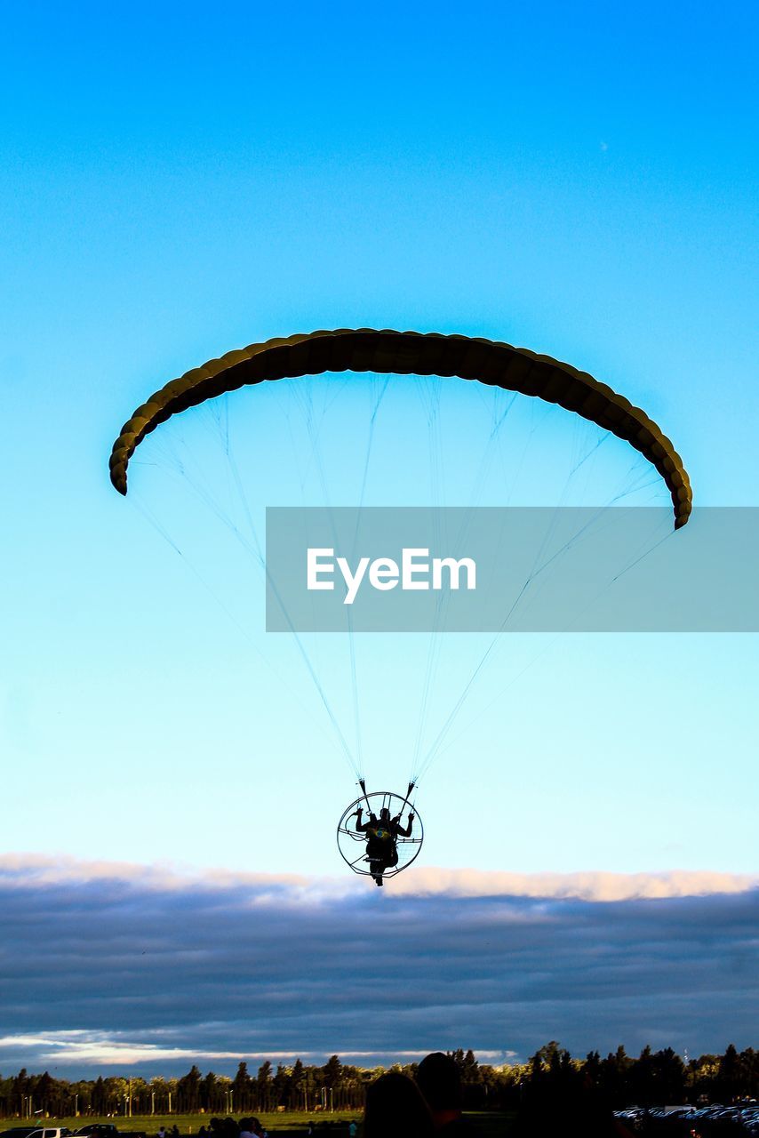 Man powered paragliding against blue sky