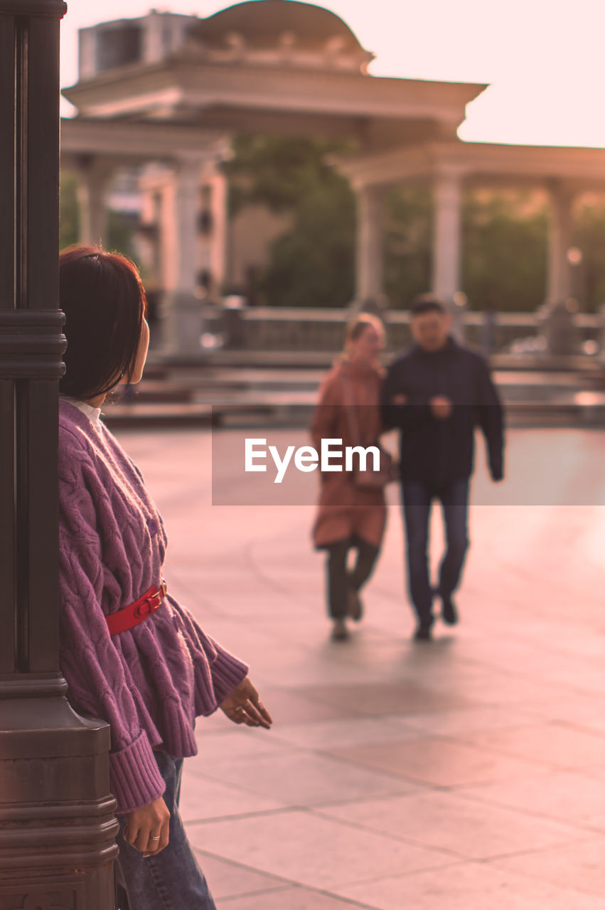 Rear view of a lone woman looking at a couple in city square