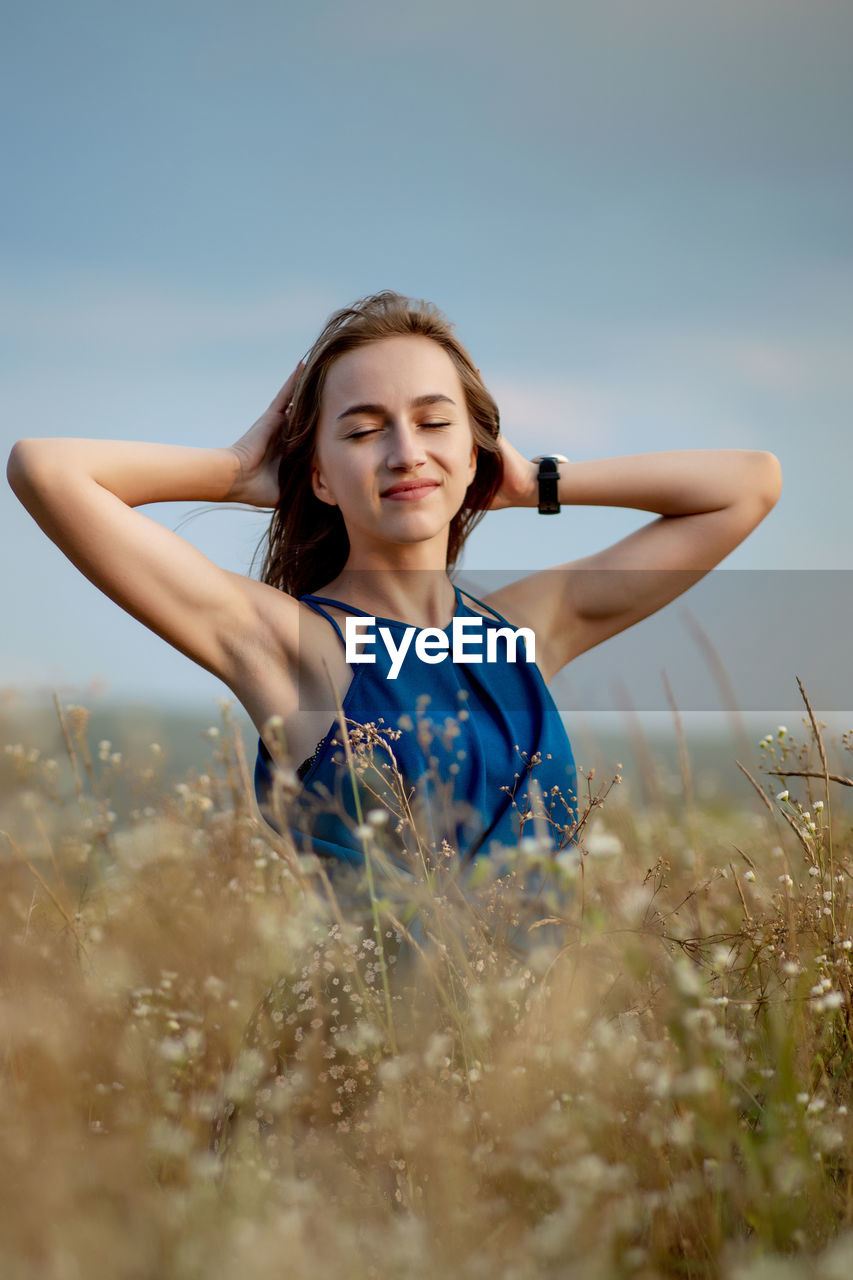 YOUNG WOMAN WITH ARMS RAISED ON FIELD