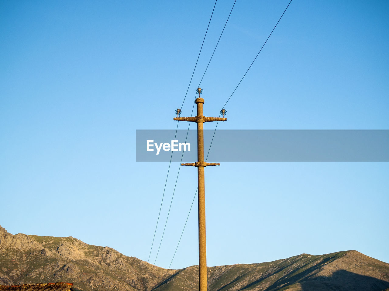 Low angle view of electricity pylon and mountains against clear blue sky