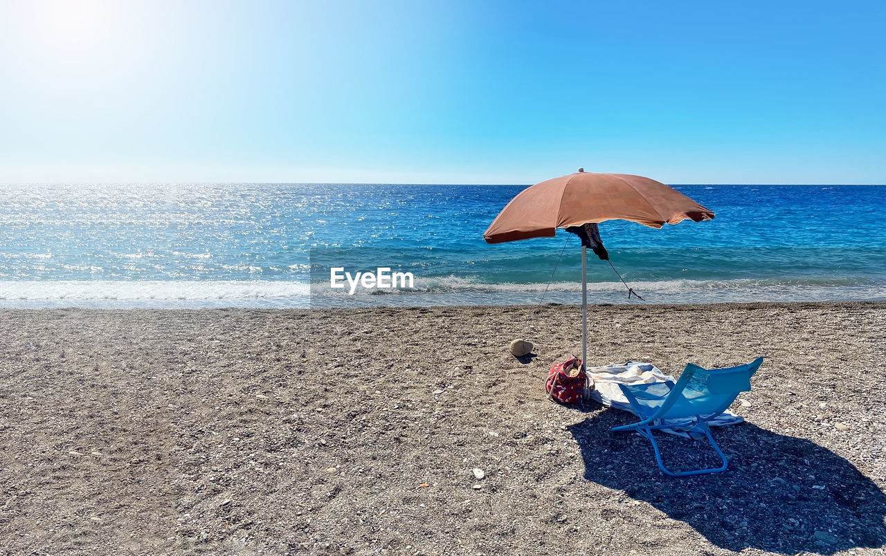 A deckchair under an umbrella facing the blue sea in a stony beach in sicily, italy. summer holidays 