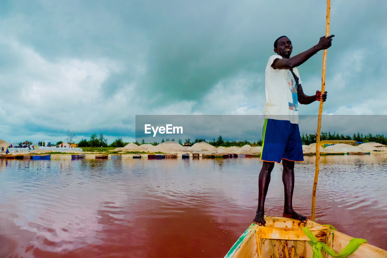 MAN STANDING AT LAKE AGAINST SKY