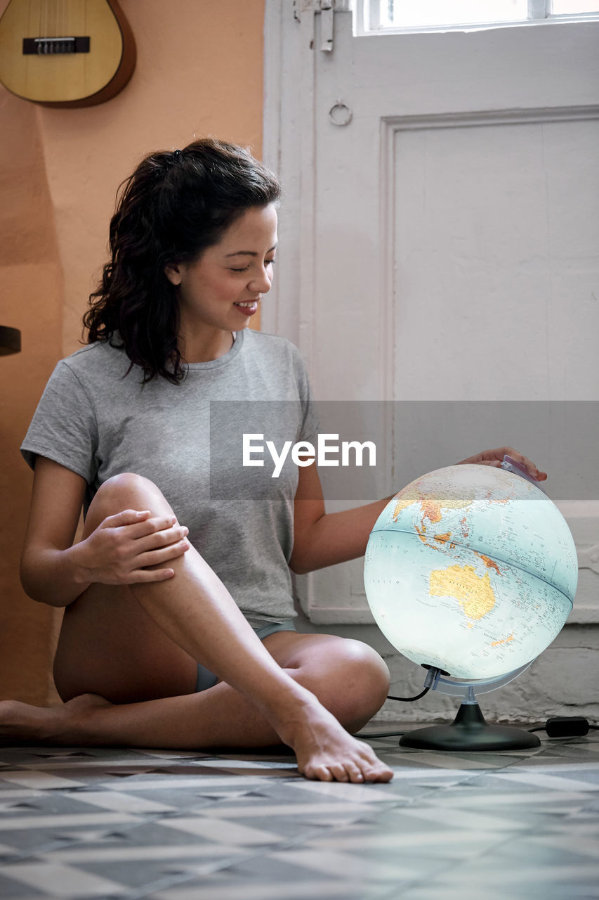 Full length of smiling woman touching globe at home