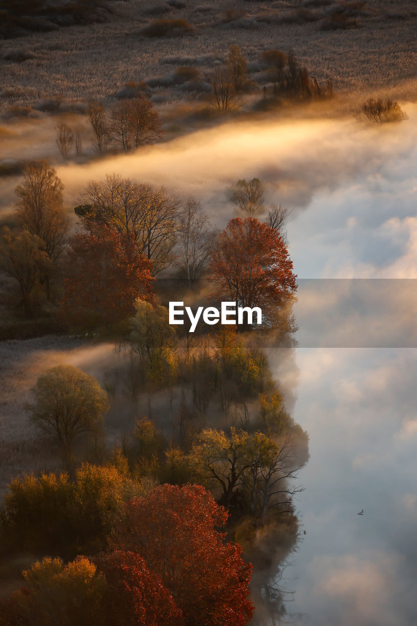 Scenic view of river against sky during sunrise, trees surrounded by clouds