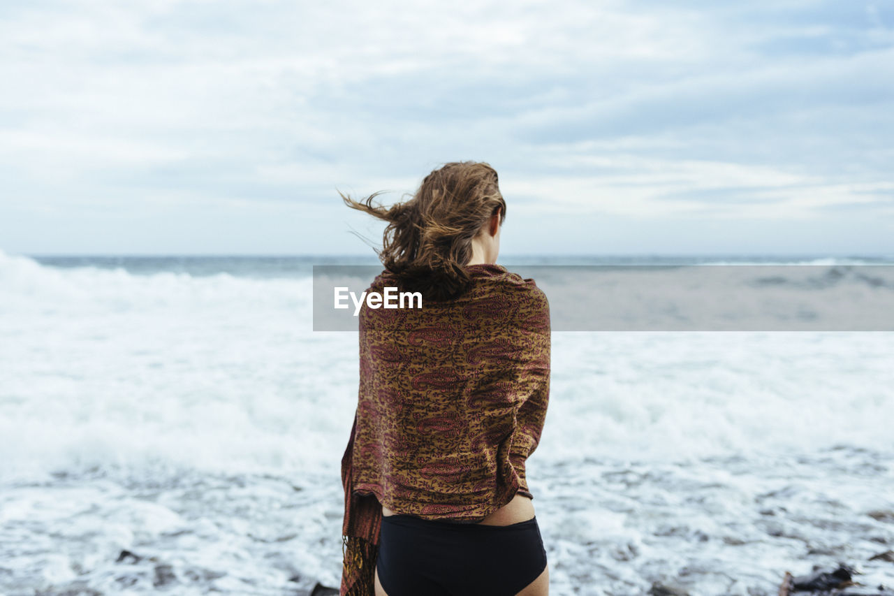 Rear view of woman standing at beach against sky