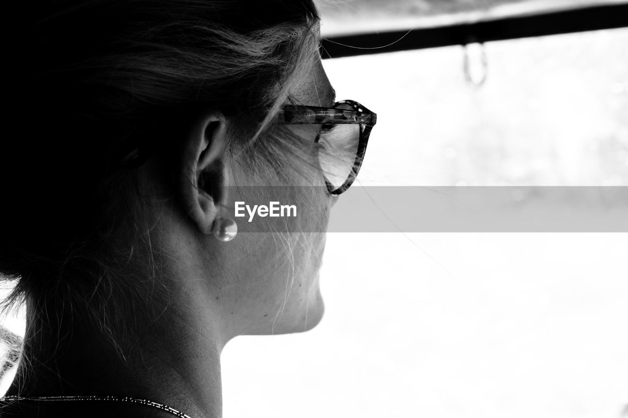 Rear view of young woman looking through wet windshield while traveling in car