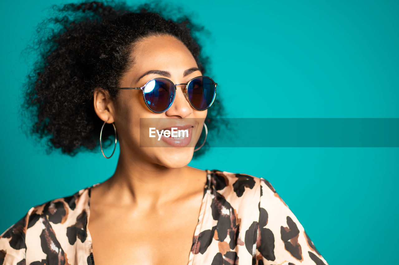 Smiling young woman wearing sunglasses against blue background