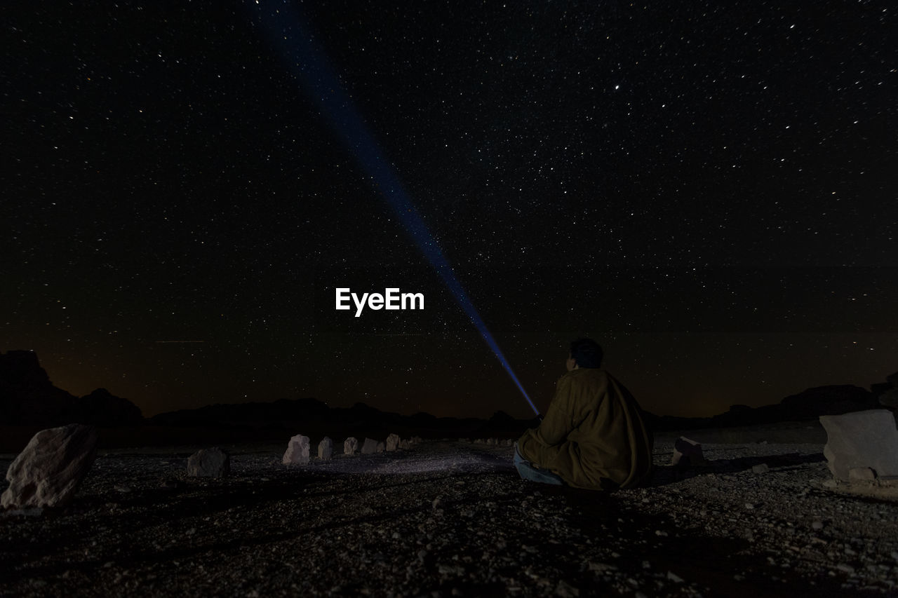 REAR VIEW OF MAN SITTING ON FIELD AGAINST CLEAR SKY AT NIGHT