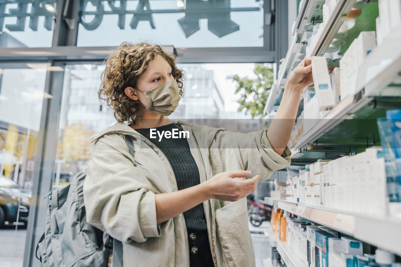 Female customer wearing protective face mask while checking medicine in chemist shop