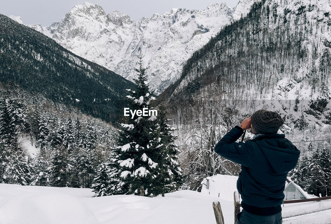 Rear view of young man taking photos of mountains in winter.
