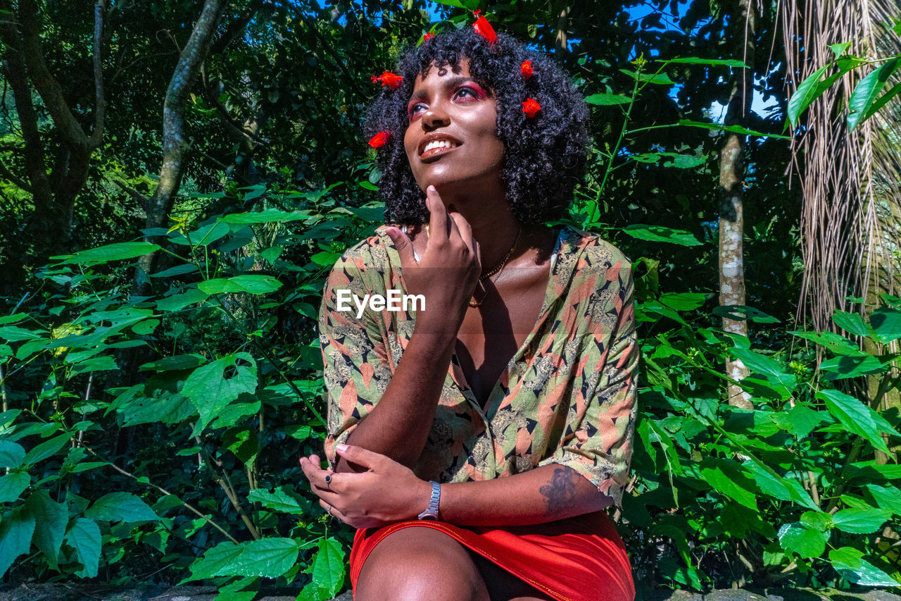 Woman wearing red flowers while looking up in forest