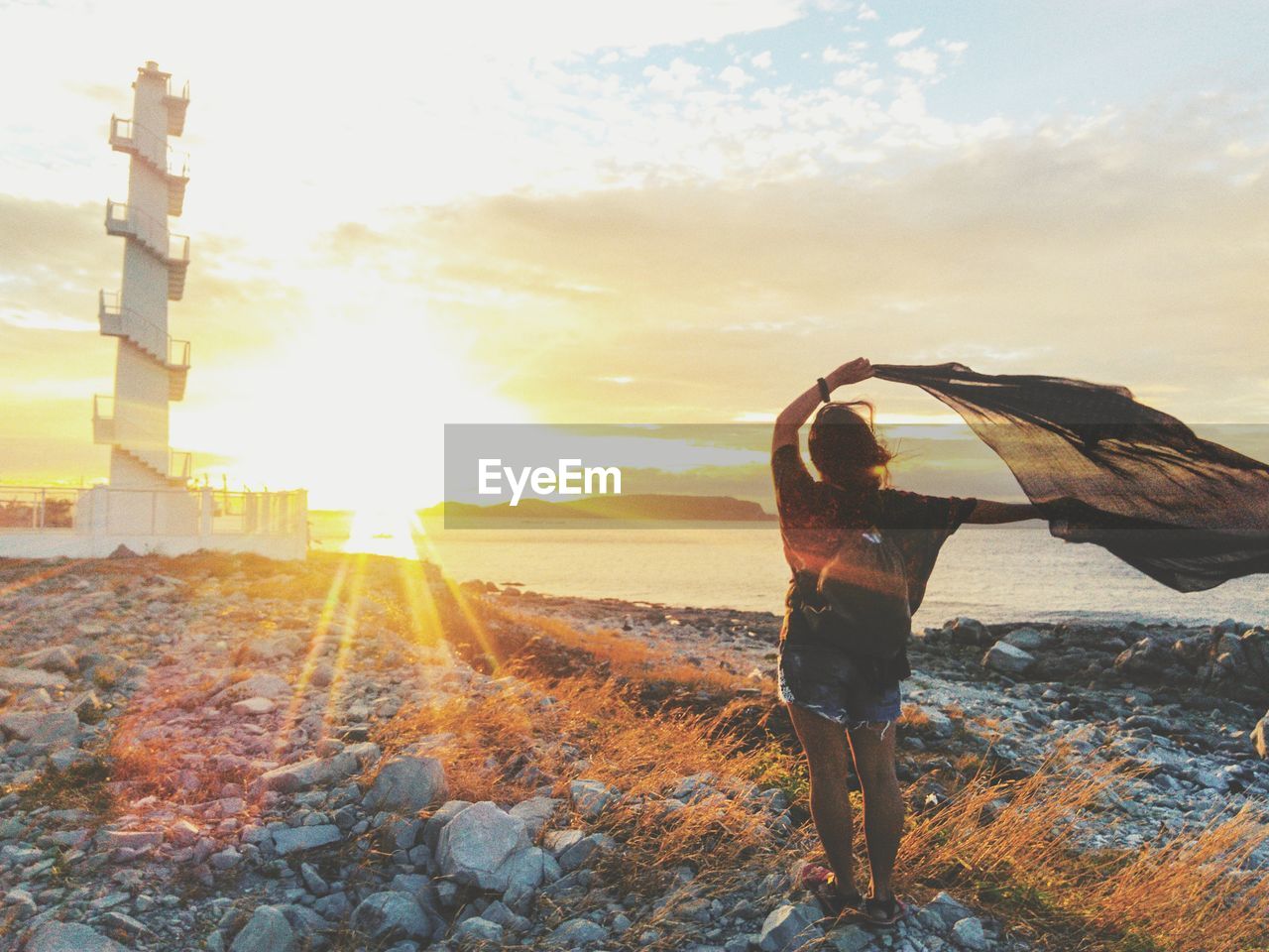 REAR VIEW OF MAN STANDING AGAINST SKY AT SUNSET