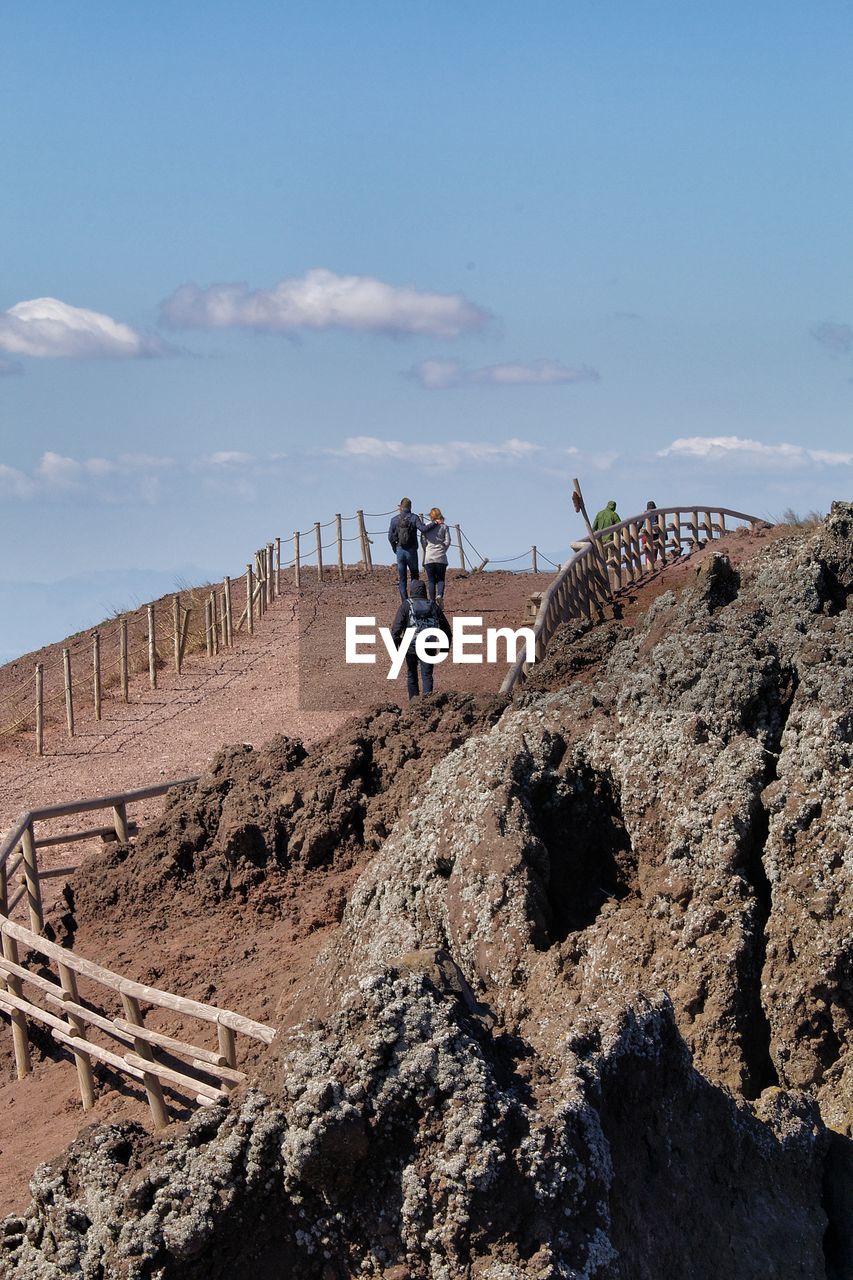 BOY STANDING ON ROCK AGAINST SKY IN BACKGROUND