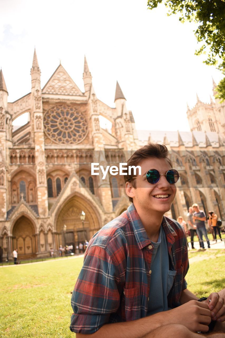 Portrait of happy man wearing sunglasses while sitting against westminster abbey