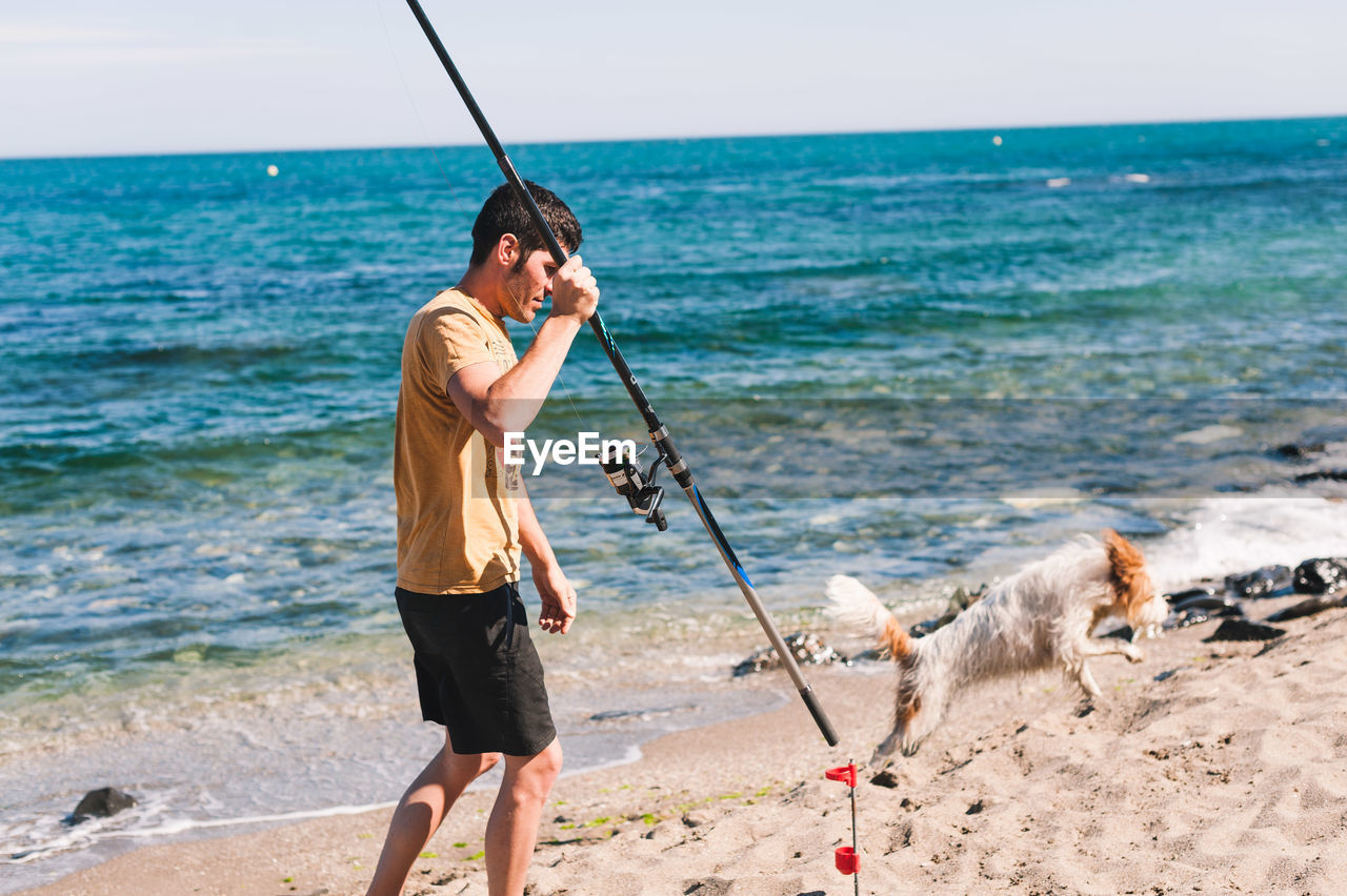 FULL LENGTH OF MAN WITH DOG STANDING ON BEACH