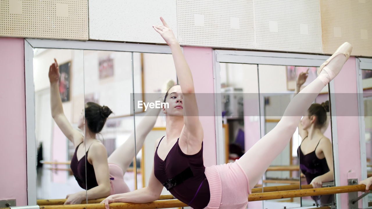 In dancing hall, young ballerina in purple leotard performs elegantly a certain ballet exercise