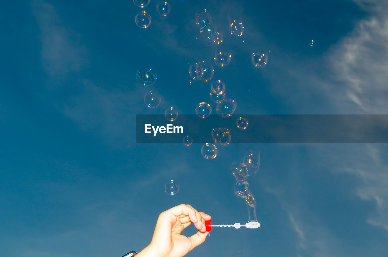 Low angle view of person making bubbles against sky