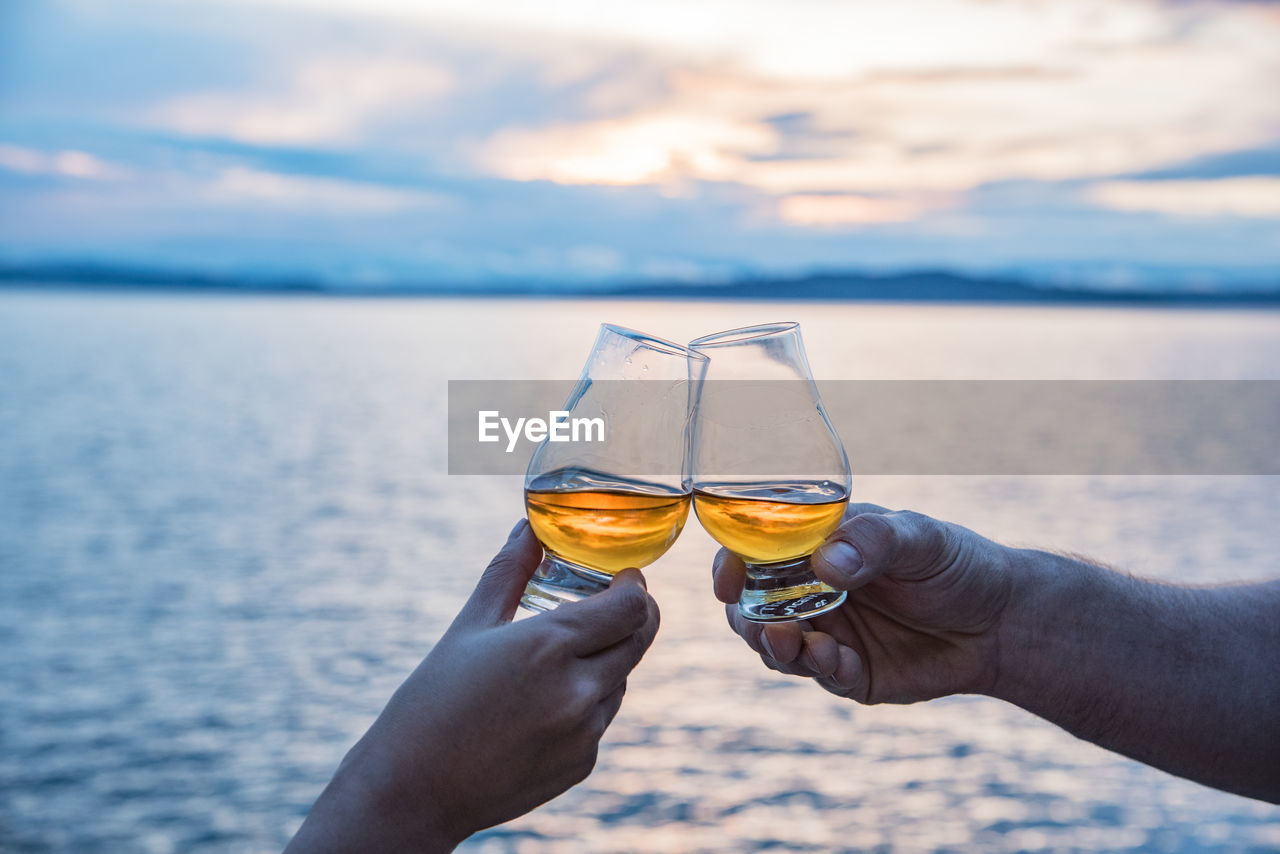Close-up of hands toasting glasses against the lake