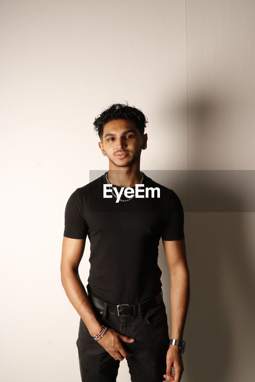 one person, portrait, black, adult, looking at camera, t-shirt, sleeve, young adult, indoors, front view, standing, three quarter length, photo shoot, men, copy space, studio shot, lifestyles, casual clothing, clothing, fashion, cool attitude, serious, athlete, sports, black hair, spring, relaxation, strength