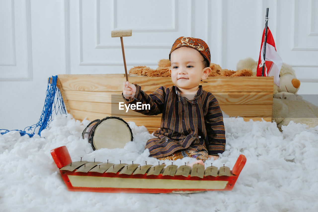 
a baby boy wearing javanese traditional clothes while playing javanese musical instruments