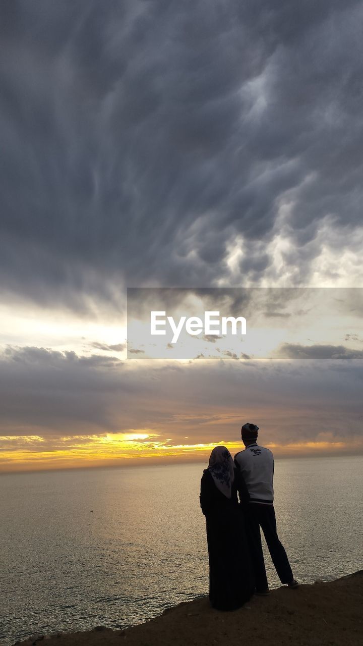 A couple standing on beach against sky during sunset