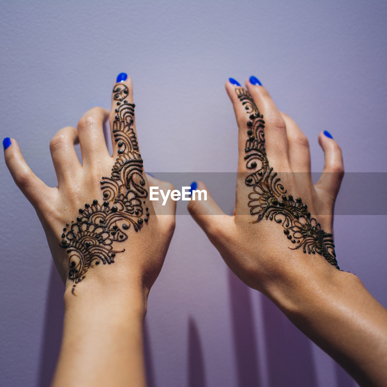 Cropped hands of woman with henna tattoo by wall