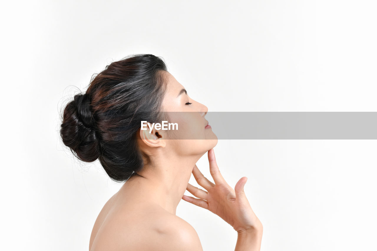 Side view of shirtless woman with eyes closed against white background