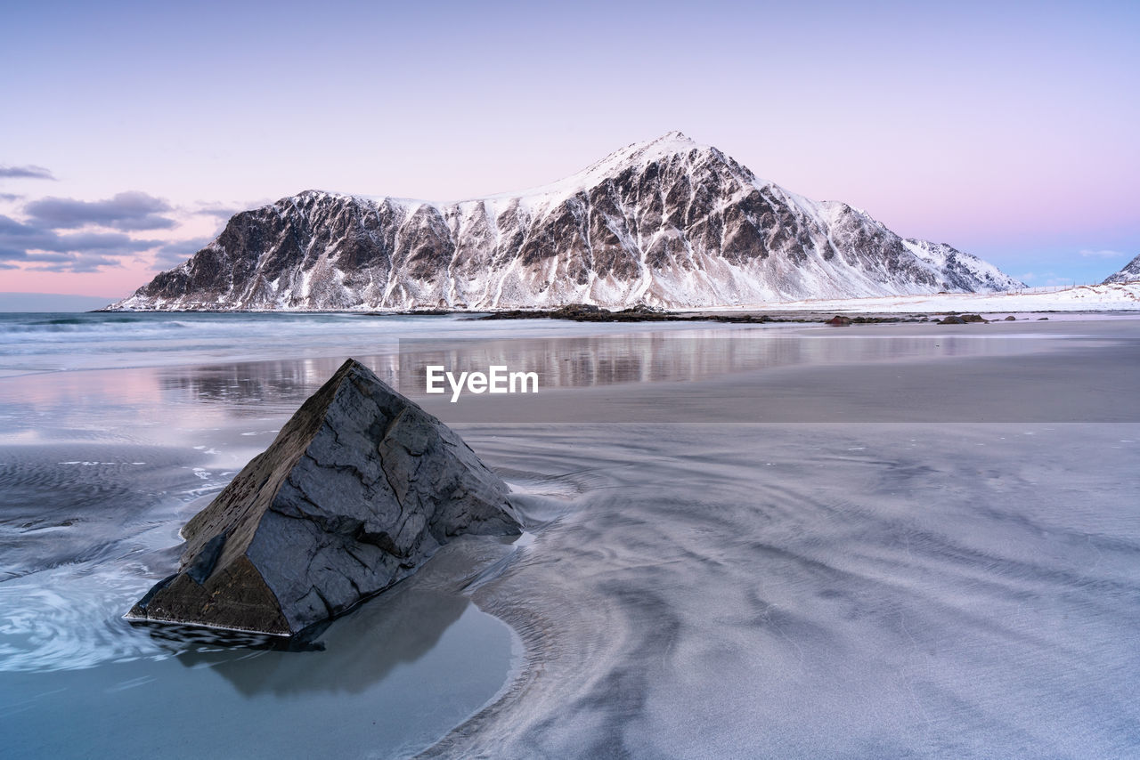 Scenic view of sea by snowcapped mountains against sky during sunset