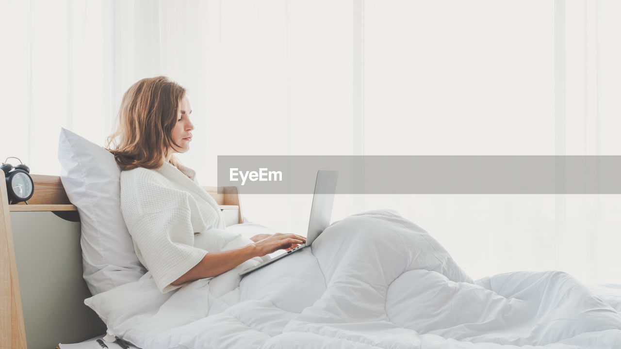 Young woman using laptop while sitting on bed at home