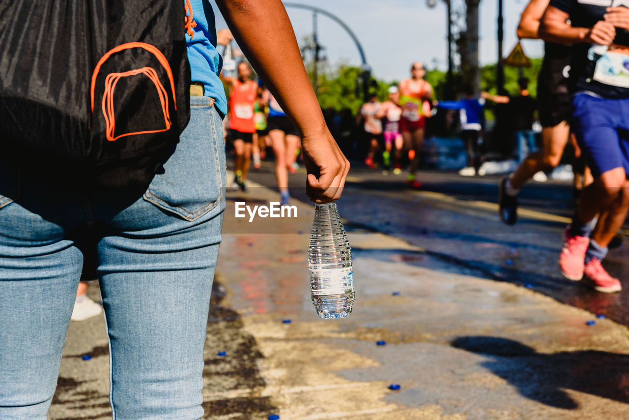 Midsection of woman holding water bottle while standing on road