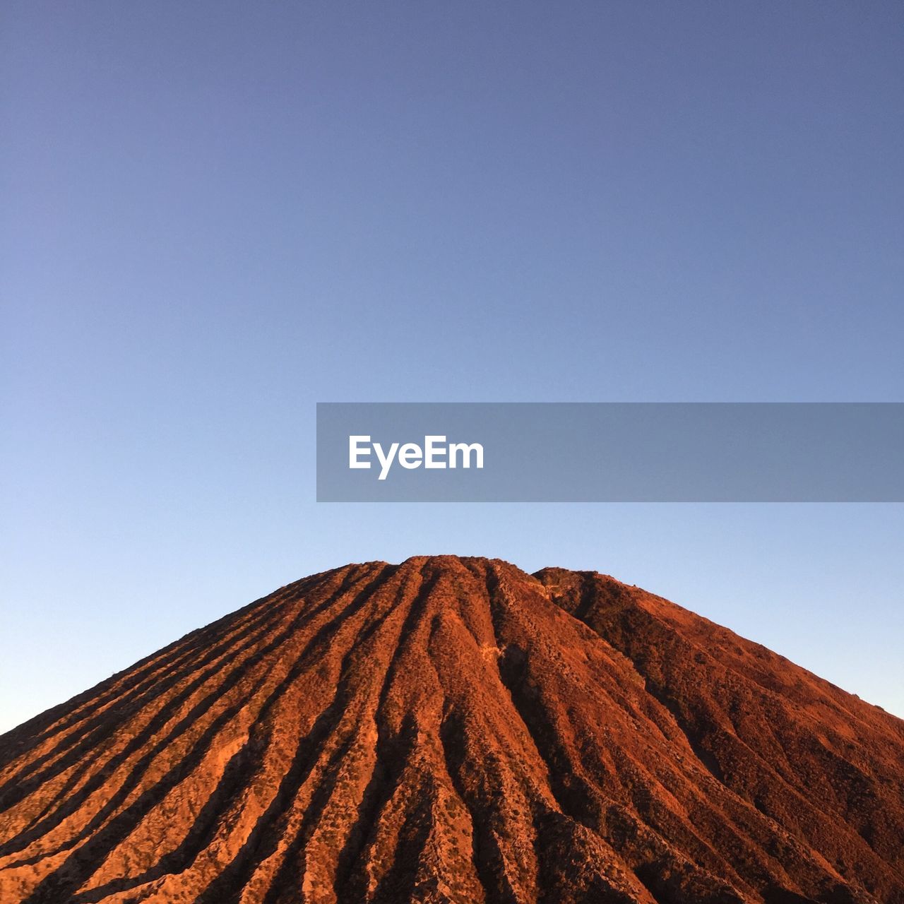 Low angle view of volcanic mountain against clear blue sky