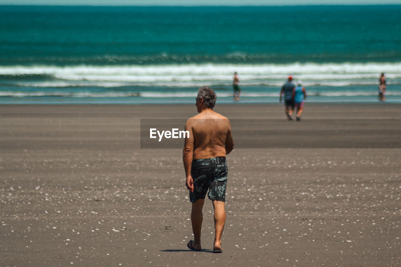 Rear view of shirtless man walking on beach