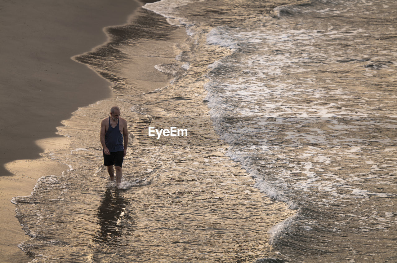 Adult man walking on a beach with ocean wave during sunrise