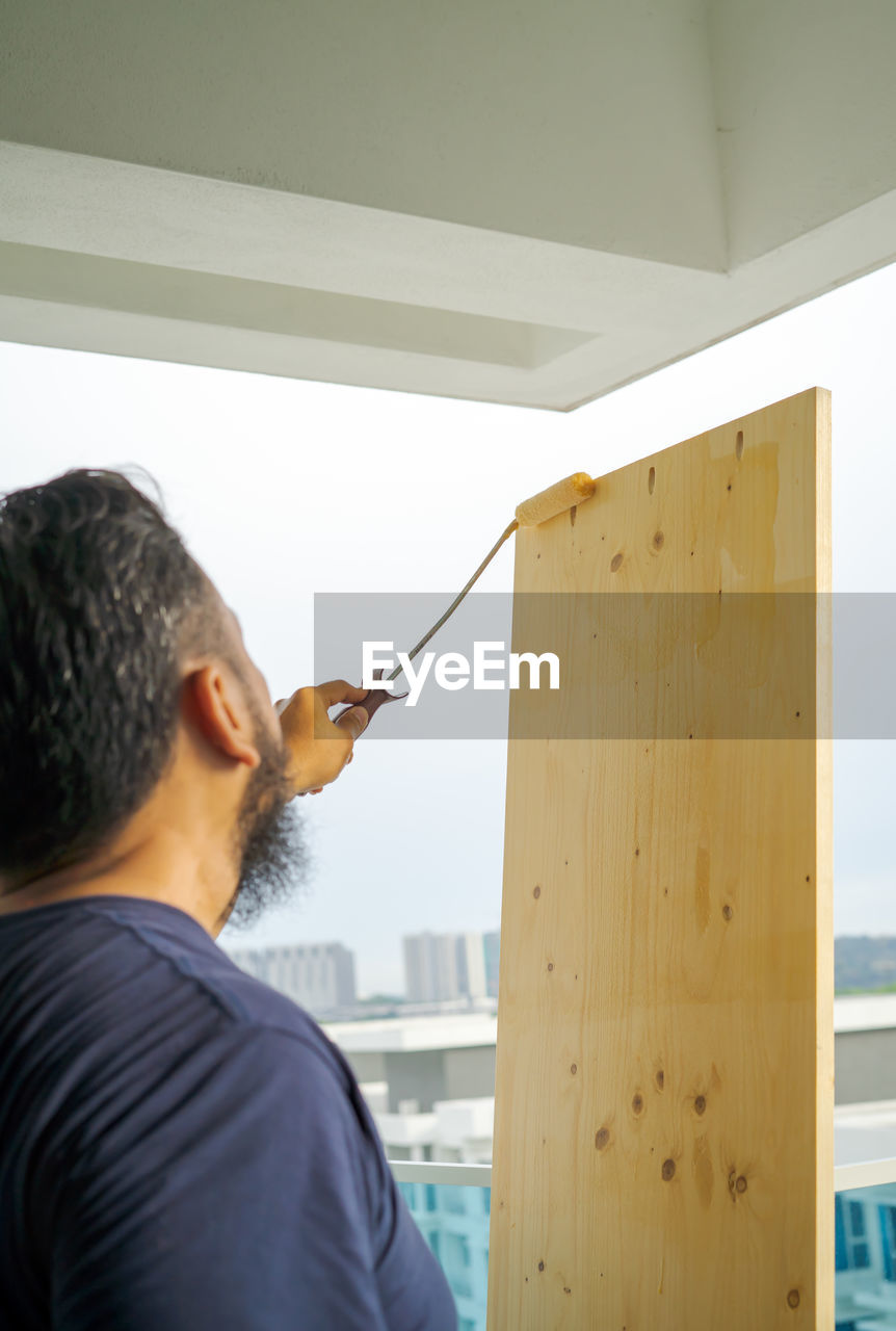 Applying clear coat paint on a wooden surface with roller brush. painting wood wall and floor.