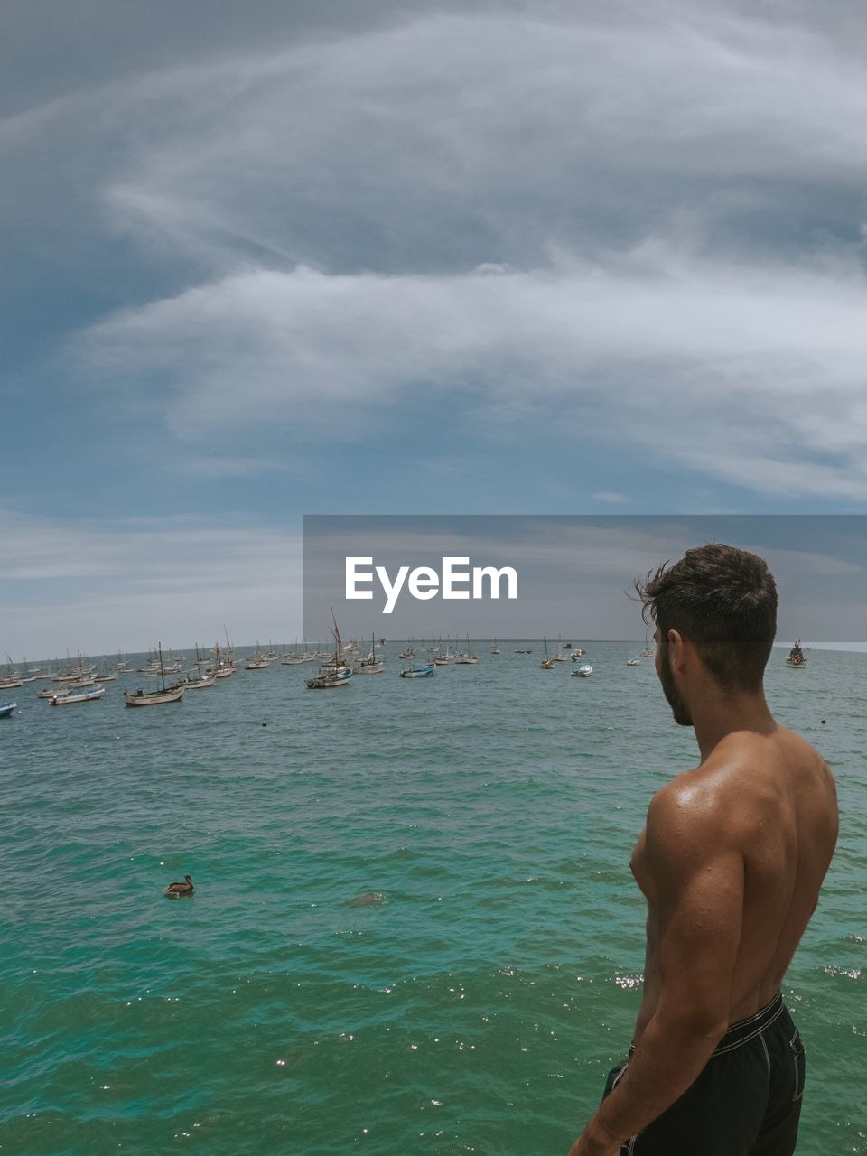 Rear view of shirtless man looking at sea against sky