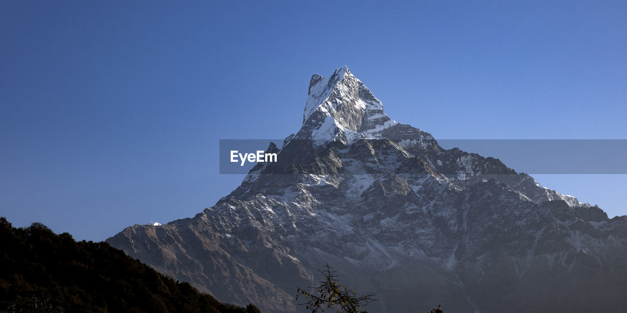 Low angle view of snowcapped mountains against clear blue sky