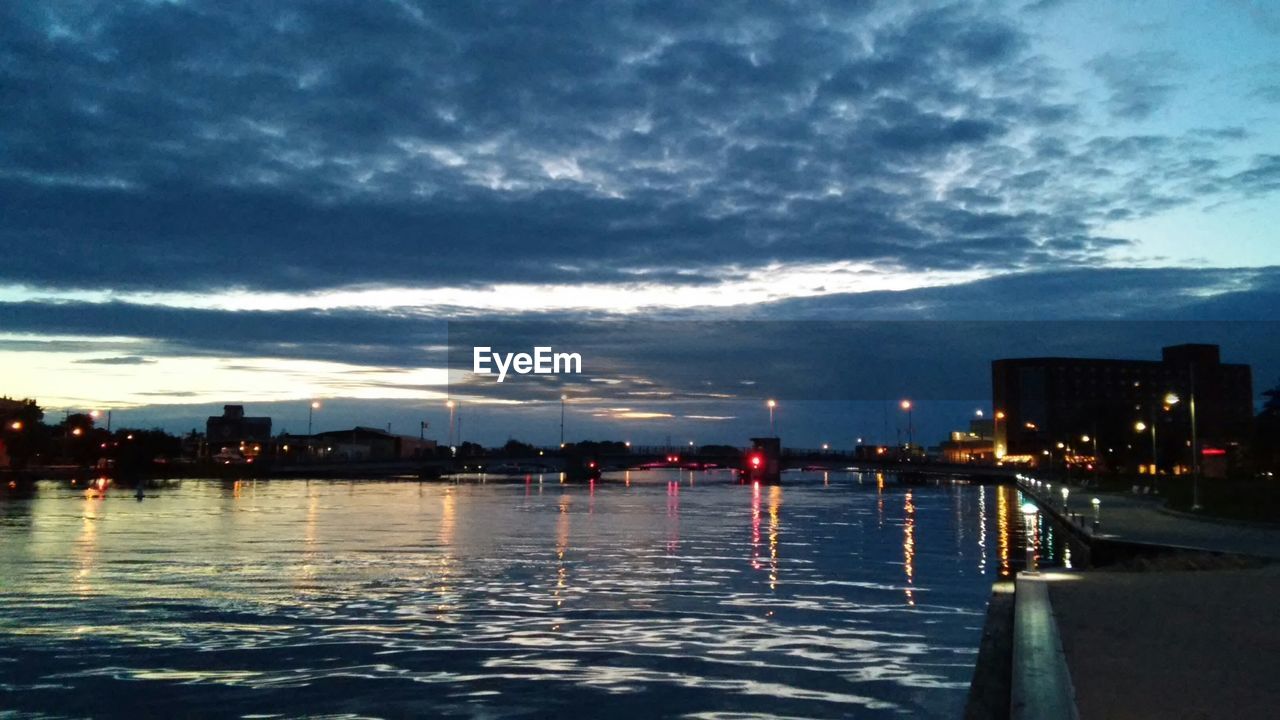 VIEW OF ILLUMINATED CITYSCAPE AGAINST CLOUDY SKY AT DUSK