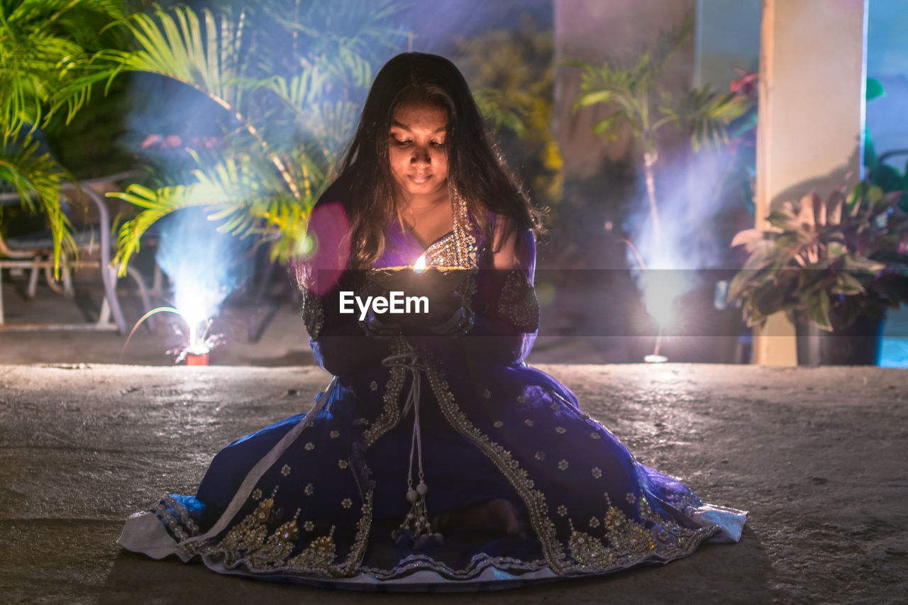 PORTRAIT OF WOMAN SITTING AT ILLUMINATED PARK