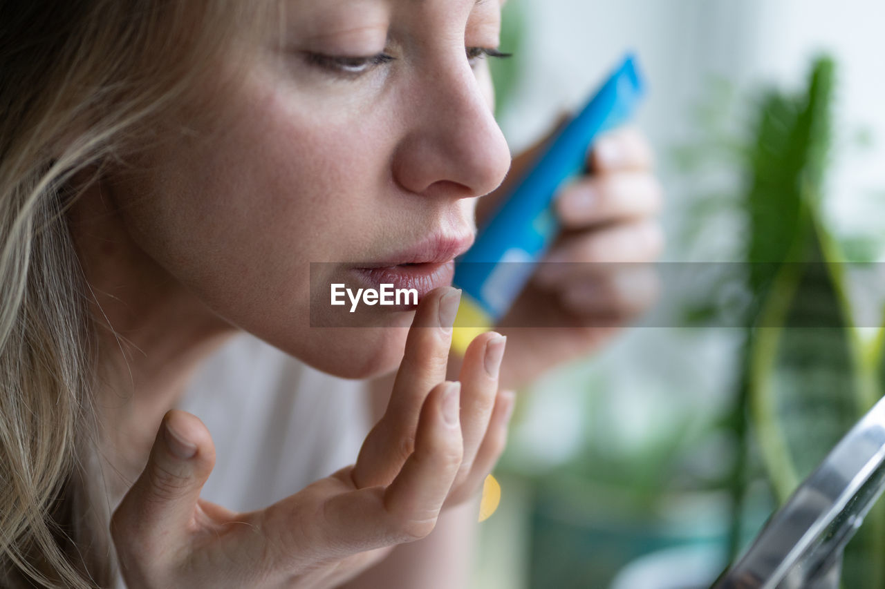 Woman applying lipstick by mirror on table