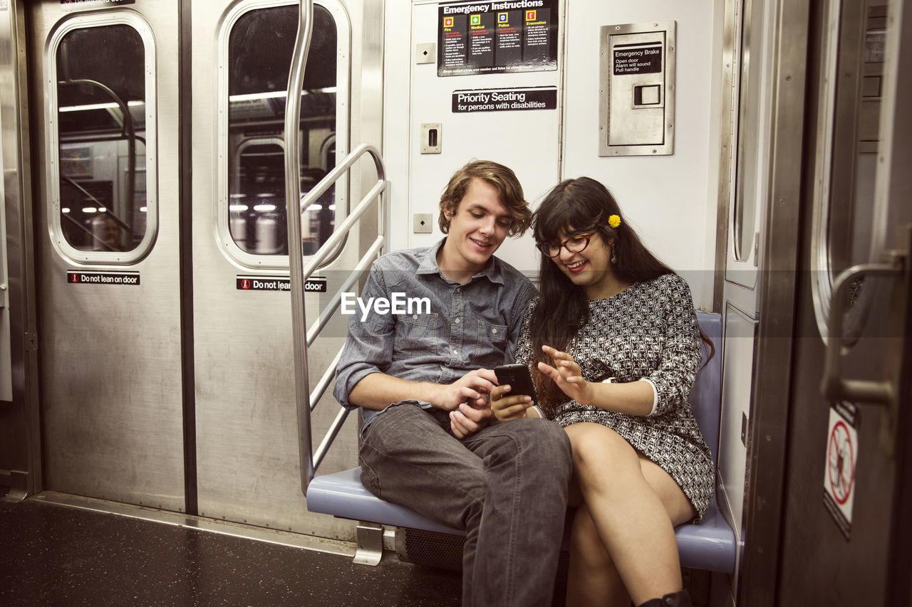 Happy couple looking at smart phone while sitting in subway train