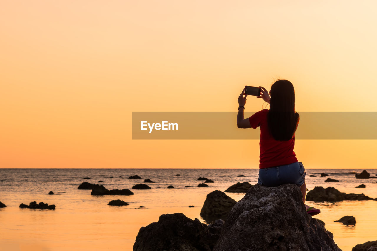 Man photographing sea against sky during sunset