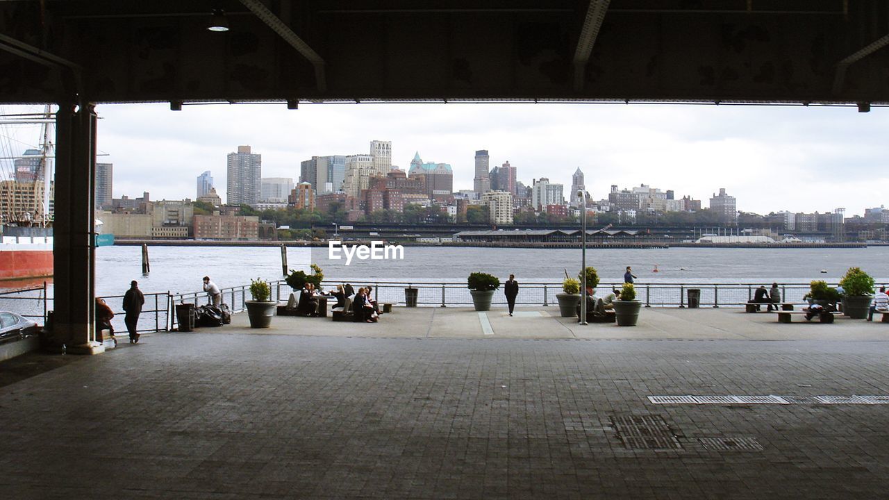 GROUP OF PEOPLE IN CITY BY RIVER AGAINST BUILDINGS